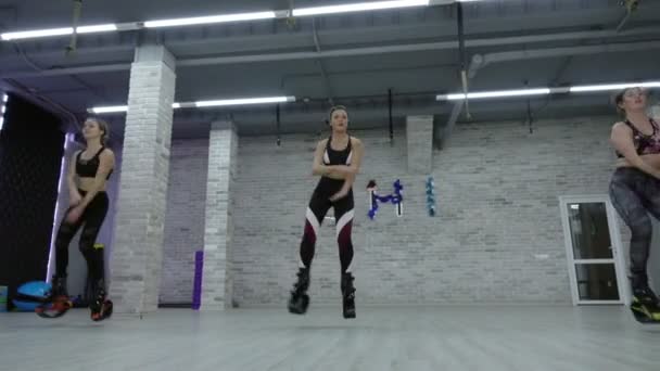 Een vrouwelijke groep van drie jonge, sexy meisjes Kangoo Jumps in de sportschool. — Stockvideo