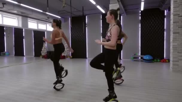 A female group of three young, sexy girls Kangoo Jumps in the gym. — Stock Video