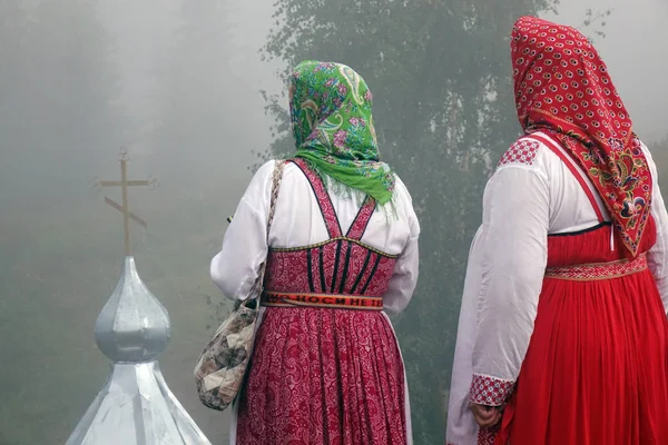 Two women in traditional Slavic costumes, standing on a hill, looking at the dome of the Church . — Stock Photo, Image