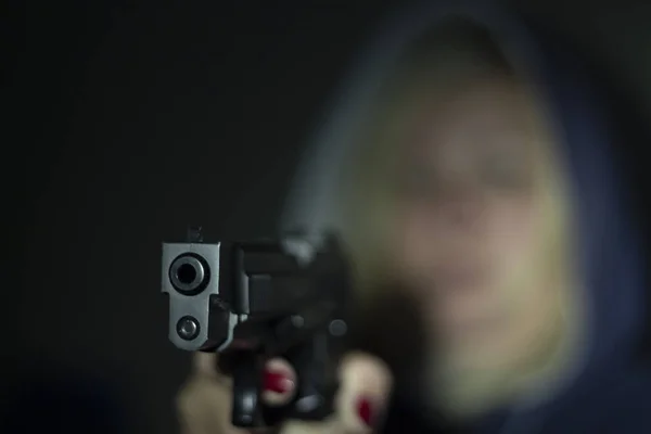 En kvinna håller en pistol i handen och pekar det på kameran. Fokusera på framsidan av pistolen. — Stockfoto