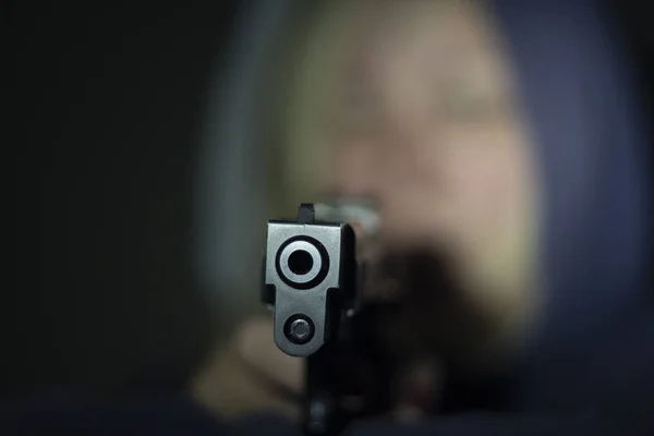A woman holds a gun in her hand and points it at the camera . Focus on the front of the gun. — Stock Photo, Image