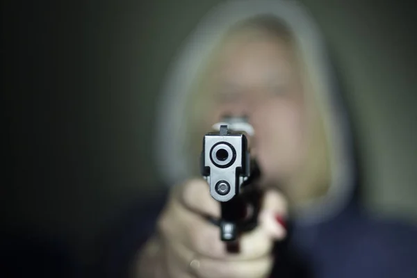 A woman holds a gun in her hand and points it at the camera . Focus on the front of the gun. — Stock Photo, Image