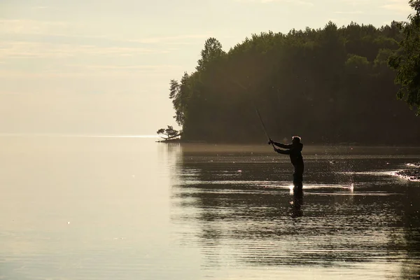 Silhueta de um pescador ao pôr-do-sol. Pesca no lago . — Fotografia de Stock