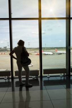 Elinde akıllı telefon olan genç bir kadın, havaalanında bir siluet . Uçak arka planda. Hava taşımacılığı kavramı.