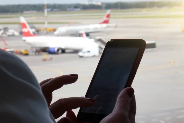 Молодая женщина со смартфоном в руках пишет сообщение, силуэт в аэропорту. Самолет на заднем плане. Концепция воздушного транспорта . — стоковое фото