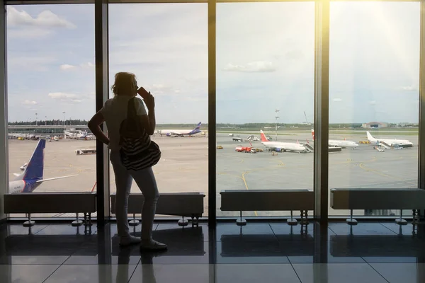 Молодая женщина со смартфоном в руках, силуэт в аэропорту. Самолет на заднем плане. Концепция воздушного транспорта . — стоковое фото