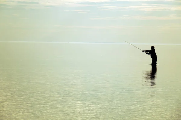 Silhouette eines Fischers bei Sonnenuntergang. Angeln auf dem See. — Stockfoto