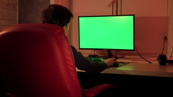 A teenager in a red chair in front of a green computer screen. — 图库视频影像