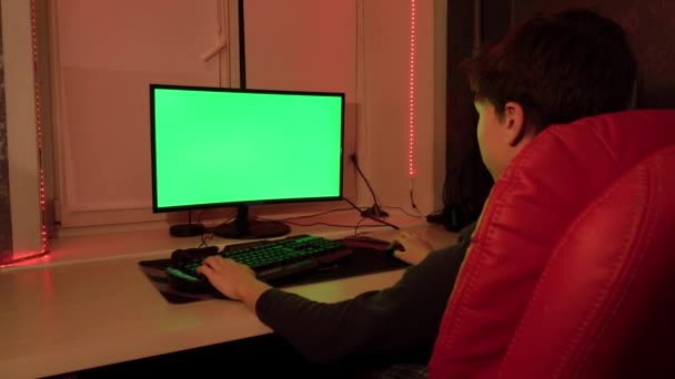 Un adolescente su una sedia rossa davanti allo schermo di un computer verde . — Video Stock