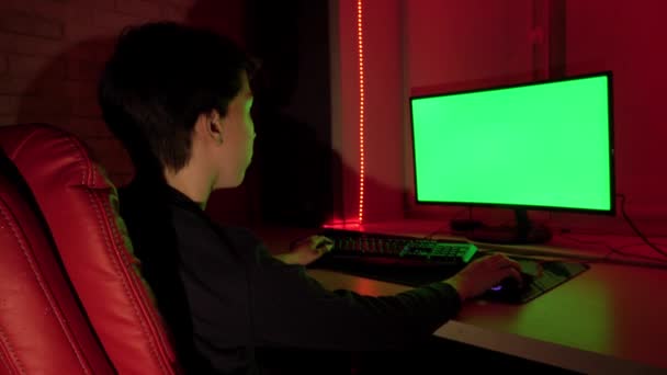 Un adolescent dans une chaise rouge devant un écran d'ordinateur vert . — Video