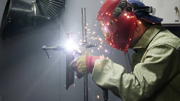 Welder in the mask. The metal product is welded by welding machine .