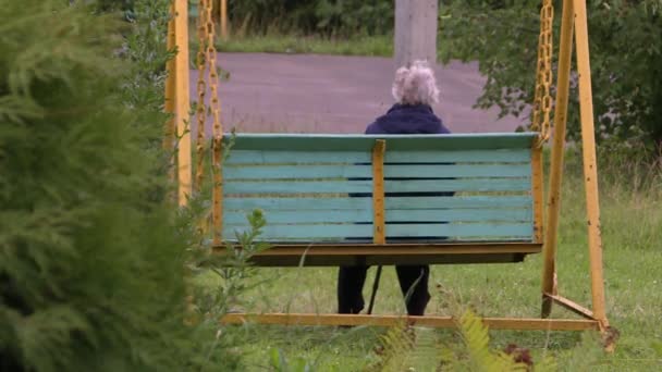 Een oudere vrouw zittend op een tuin schommel in de herfst en bewolkte dag. — Stockvideo