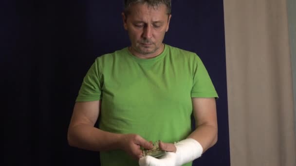 En man med en arm i gips håller pengar från kostnaden för akutsjukvård på ett sjukhus . — Stockvideo