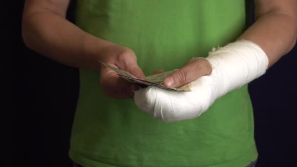 Un hombre con un brazo en un yeso mantiene el dinero del costo y el gasto de la atención médica de emergencia en un hospital  . — Vídeos de Stock