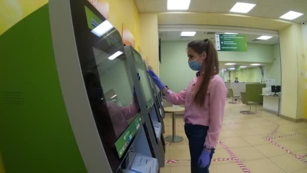 Una ragazza con una maschera medica preleva denaro da un bancomat . — Video Stock