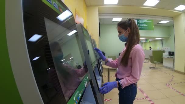 Una ragazza con una maschera medica preleva denaro da un bancomat . — Video Stock