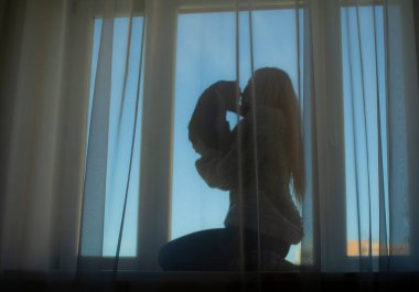 Saçları dökülmüş ve penceresinde siyah bir kedi yavrusu olan bir kızın silueti..