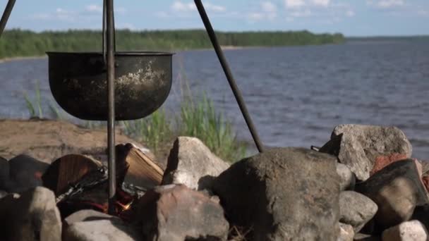 Uma panela no fogo junto ao lago. Acampar com uma panela sobre um fogo ardente. — Vídeo de Stock