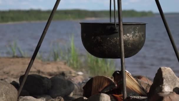 Каструля на вогні біля озера. Кемпінг з горщиком над палаючим вогнем . — стокове відео