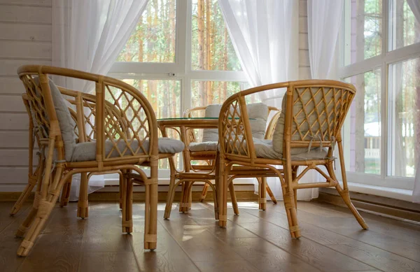 Rattan furniture on the summer porch. Outside the window is a pine forest