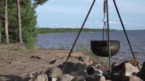 Kruka på elden vid sjön. Camping med en gryta över en brinnande eld. — Stockvideo