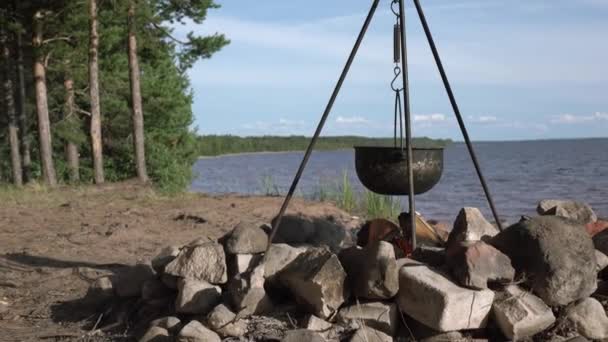 Uma panela no fogo junto ao lago. Acampar com uma panela sobre um fogo ardente. — Vídeo de Stock