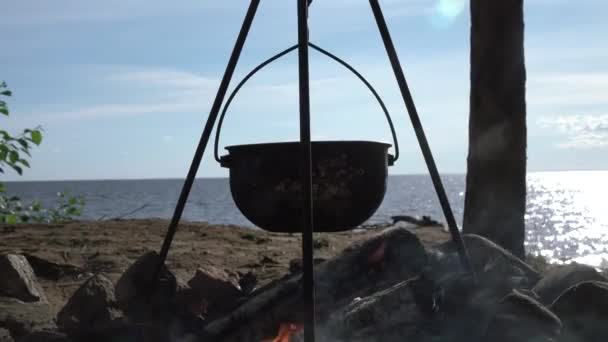 Uma panela no fogo junto ao lago. Acampar com uma panela sobre um fogo ardente. — Vídeo de Stock