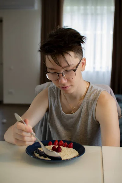 A teenager eats oatmeal porridge with berries. — Stock Photo, Image