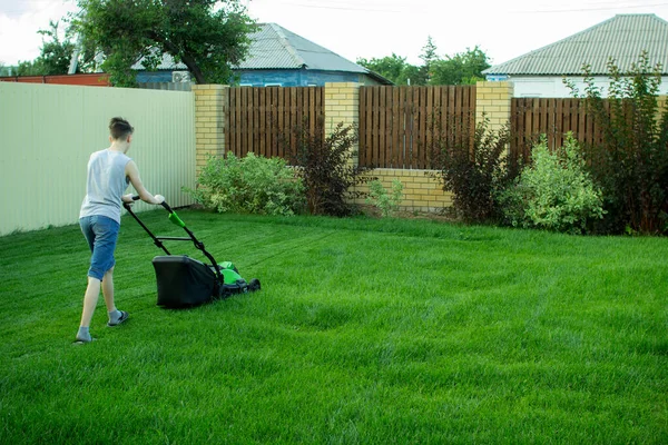 Un adolescent tond la pelouse avec une tondeuse à gazon. — Photo