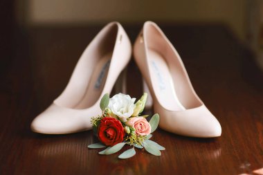 Düğün aksesuarları buket kırmızı, beyaz ve pembe çiçekler damat için ve bej ayakkabılar koyu ahşap arka planda.