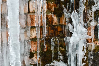 Yakın plan buz sarkıtları, buz demetleri ve sarkıtlar, çatlak buz, yosun ve çalıların dalları ile soyut eski tuğla duvar arkaplanı.