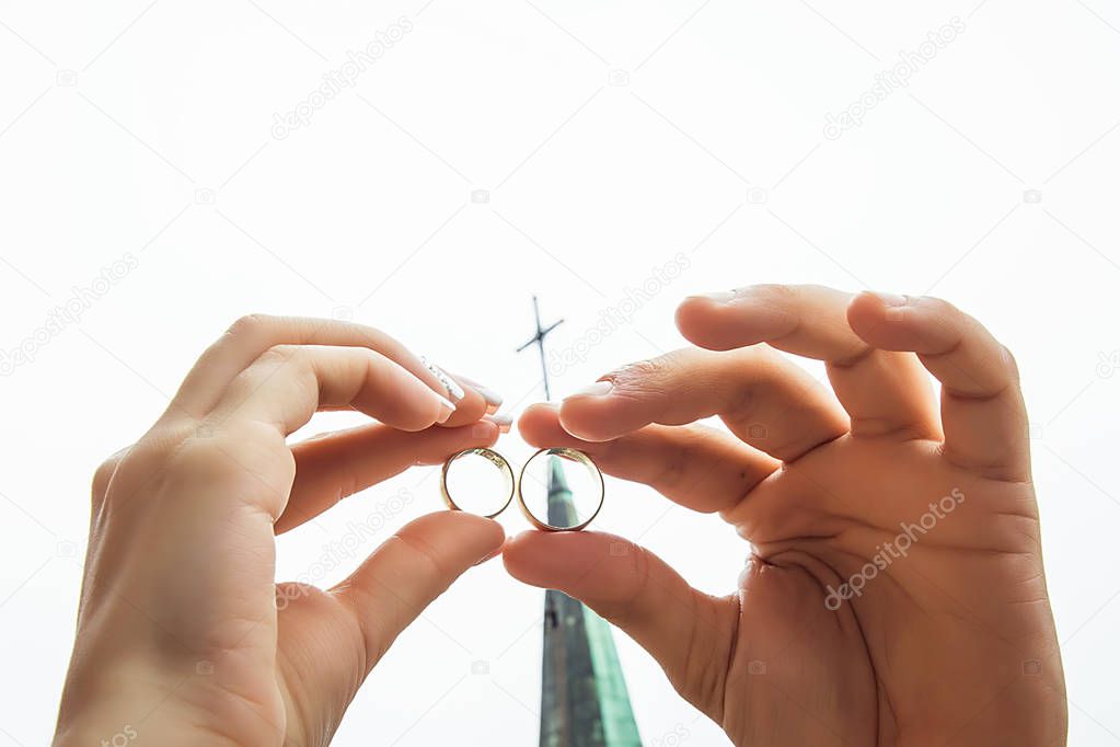 golden wedding rings in the hands of the bride sheltered against each other against the backdrop of the church dome with a cross.