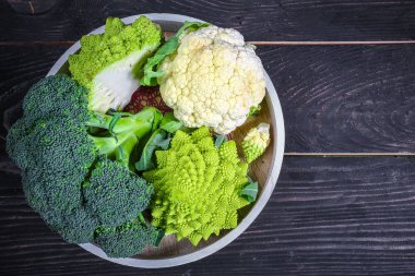 Cruciferous sebzeleri. Romanesco, karnabahar ve brokoliyi tahta arka planda yuvarlak bir tepside. Düz yatıyordu. Üst görünüm.