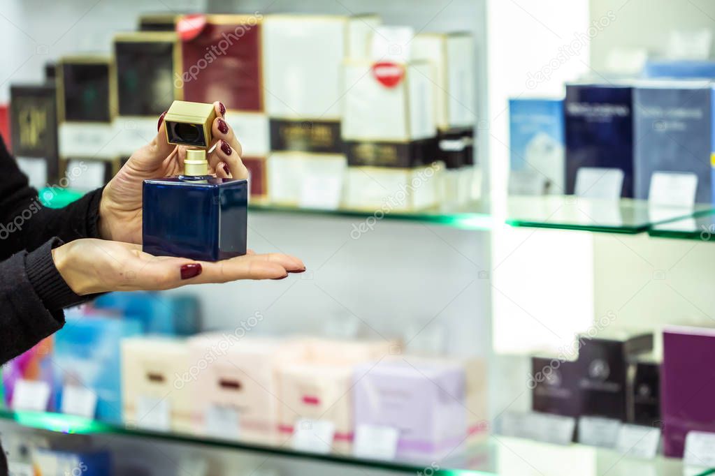 close-up hands with bottle of perfume seller. saleswoman offering new fragrance in perfume shop.