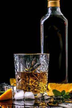 Konyak bardakları ve şişelerle dolu bir hayat, siyah arka planda portakallı meyve atıştırmalıkları. Boşluğu kopyala.