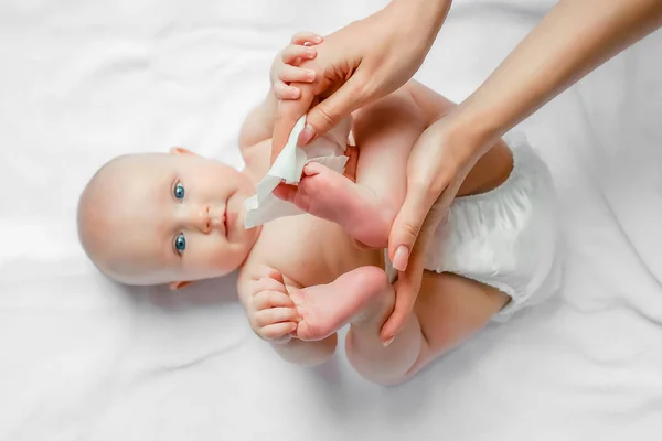 白い背景に慎重にぬれたワイプで赤ちゃんの肌のボディと脚を拭く若いお母さん コンセプトクリーニング — ストック写真