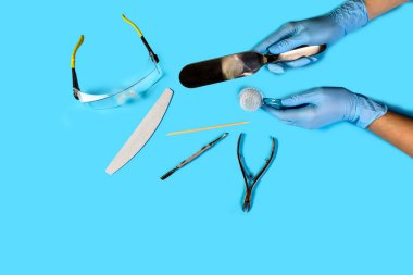 Manikür aleti ustanın elinde. Mavi arkaplan görünümlü pedikür aksesuarları. Kopya uzayı ile düz konum. Kişisel koruyucu ekipman kavramı.