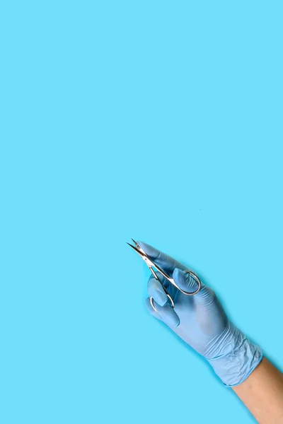 master nails in blue gloves holds manicure tool. set of manicure accessories on blue background top view. vertical image. Composition for card with a place for text.