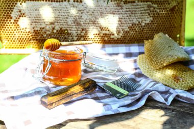 Arıcılık için çeşitli aletleri olan bir kavanoz taze bal, ahşap bir şeker kutusu ve dışarıdaki ahşap bir masada duran bir arı kovanından alınmış bir tepsi bal peteği..