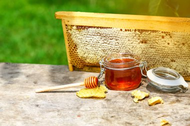 Arıcılık için çeşitli aletleri olan bir kavanoz taze bal, ahşap bir şeker kutusu ve dışarıdaki ahşap bir masada duran bir arı kovanından alınmış bir tepsi bal peteği..