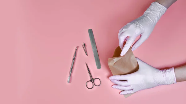 Manicure tool in the hands of the master isolated on pink background. packing a manicure tool in kraft packages before sterilizing in a dry oven. the concept of personal protective equipment.