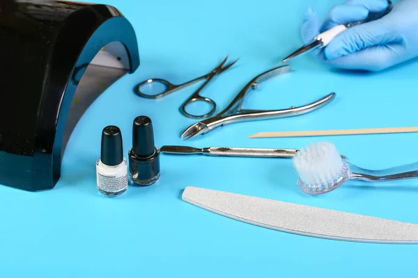 master nails in blue gloves holds manicure tool. set of manicure accessories on blue background top view. flat lay composition with copy space. the concept of healthy manicure.