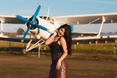 Güzel esmer, uzun siyah kıvırcık saçlı, uçağın yanında poz veren. Moda Yaşam Tarzı, Portre.