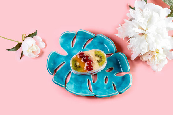 Fruit dessert cake with spring flowers of the pion on a blue ceramic plate, isolated on pink background.