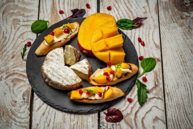 Restoran Hot Starter Food - Mangolu Camembert peyniri. Mangolu fırça, bir şist tahtasında, ahşap masa, gurme restoran aperatifleri menüsünde servis edilir..