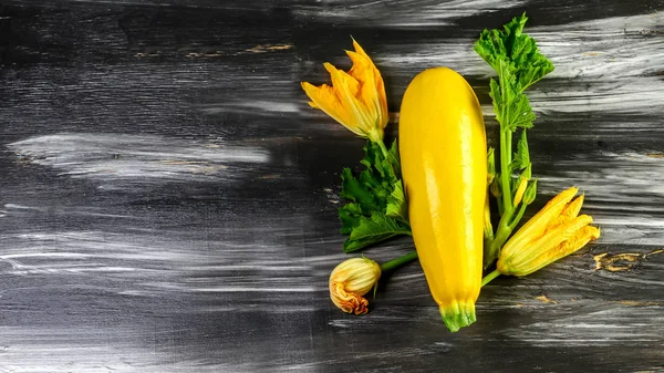 Fresh yellow zucchini with blossom on a black wooden table. Top view, place for text