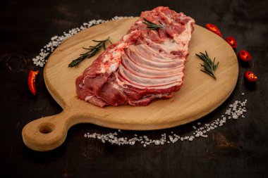 Ahşap kesim tahtasındaki çiğ pirzola, tuz, baharat ve diğer malzemeler. Siyah arkaplan, üst görünüm