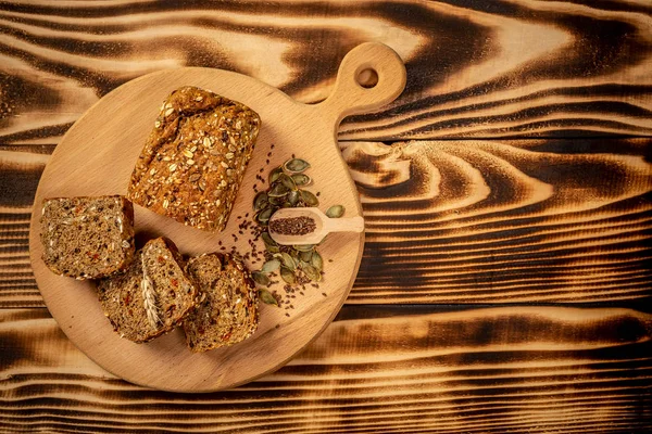 Rolo de pão integral e fatias em tábua de corte de madeira. Comida saudável. vista superior — Fotografia de Stock