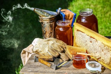 Arıcılık için çeşitli aletleri olan bir kavanoz taze bal, ahşap bir şeker kutusu ve dışarıdaki ahşap bir masada duran bir arı kovanından alınmış bir tepsi bal peteği.