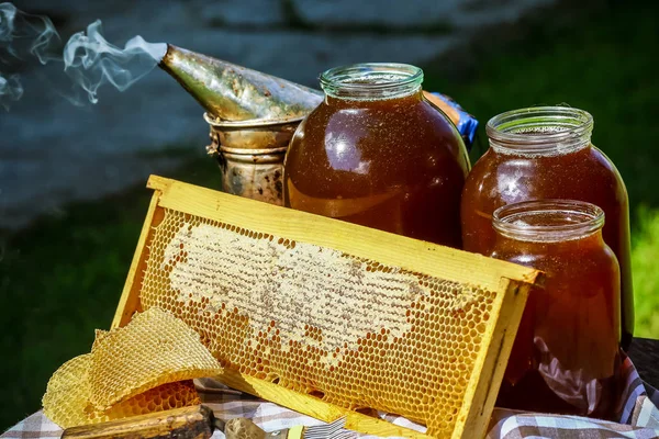 Банка свежего меда с разнообразными инструментами для пчеловодства, деревянный дозатор и поднос из пчелиного улья в натюрморте на деревянном столе на открытом воздухе с копировальным местом — стоковое фото